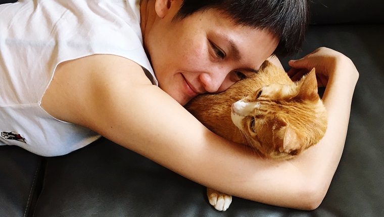 Close-Up Of Smiling Woman With Cat Lying On Sofa At Home