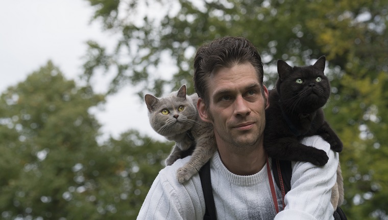 Male on a bike with 2 cats enjoying the ride on his shoulder.