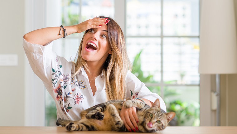 Young woman at home playing with her cat stressed with hand on head, shocked with shame and surprise face, angry and frustrated. Fear and upset for mistake.