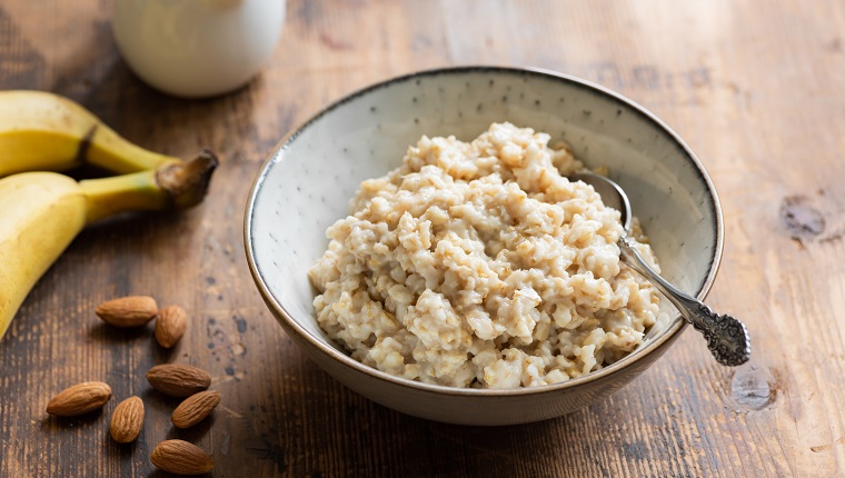 Oatmeal porridge in bowl served with banana, almonds and almond milk for healthy breakfast. Old wooden table background. Healthy lifestyle concept