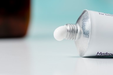 A tube of hydrocortisone cream on a domestic bathroom top with a blue background.